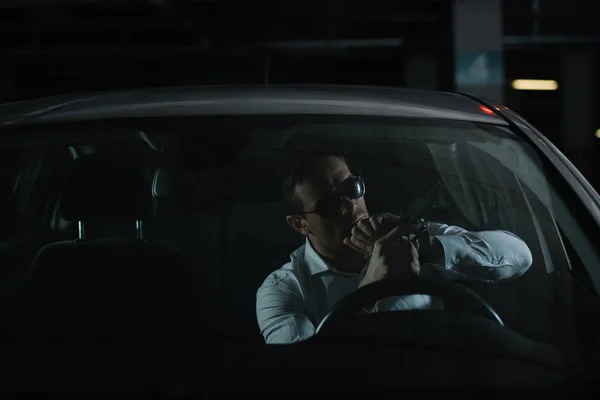 Serious male undercover agent in sunglasses charging gun in car — Stock Photo