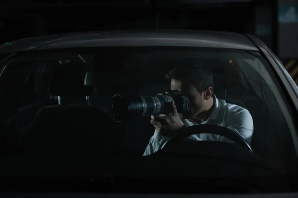 Male private detective spying by camera with object glass from his car — Stock Photo