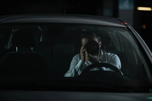 Front view of male private detective spying by camera with object glass from his car — Stock Photo