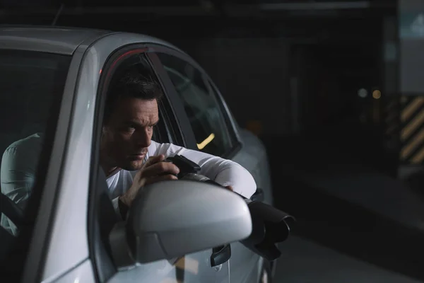 Focused male private detective doing surveillance by camera from his car — Stock Photo