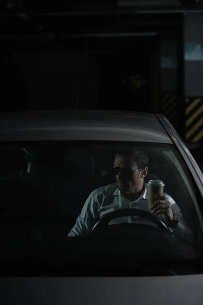 Agente sotto copertura maschile in occhiali da sole seduto in auto con tazza di carta di caffè — Foto stock