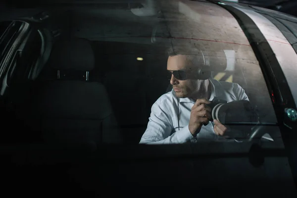 Seriöser männlicher Privatdetektiv mit Kopfhörer überwacht mit Objektglas aus dem Auto — Stockfoto