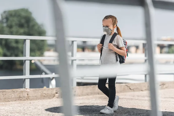 Kid in protective mask walking with school bag on bridge, air pollution concept — Stock Photo