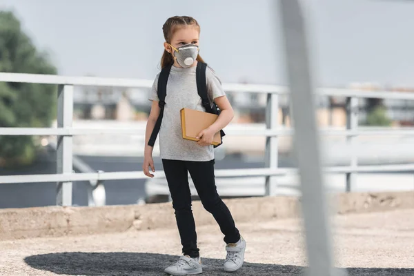 Kid in protective mask walking with book on bridge, air pollution concept — Stock Photo