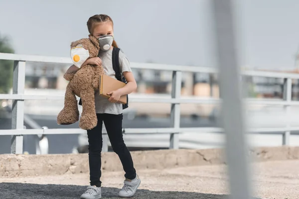 Kid in protective mask walking with teddy bear and book on bridge, air pollution concept — Stock Photo