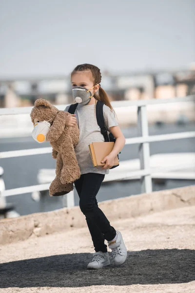 Child in protective mask holding teddy bear and book on bridge, air pollution concept — Stock Photo