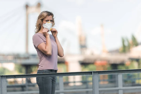 Mujer con máscara protectora en el puente y mirando hacia otro lado, concepto de contaminación del aire - foto de stock