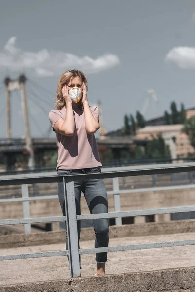 Woman in protective mask standing on bridge and touching head, air pollution concept — Stock Photo