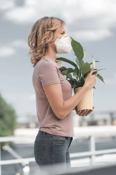 Side view of woman in protective mask holding potted plant on bridge, air pollution concept — Stock Photo