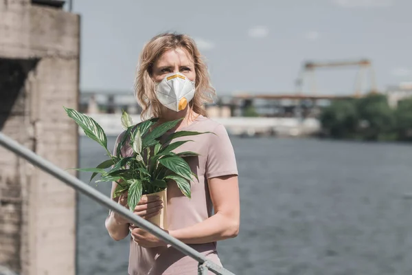 Woman in protective mask holding potted plant on bridge, air pollution concept — Stock Photo