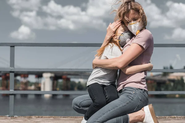 Mother and daughter in protective masks hugging on bridge, air pollution concept — Stock Photo