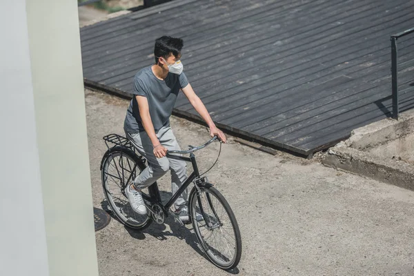 High angle view of asian teen in protective mask riding bicycle in city, air pollution concept — Stock Photo