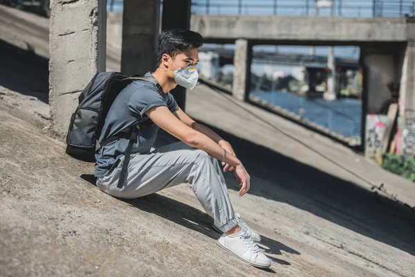Side view of asian teen in protective mask sitting under bridge, air pollution concept — Stock Photo
