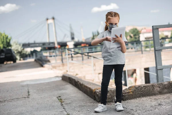 Child in protective mask using tablet, air pollution concept — Stock Photo