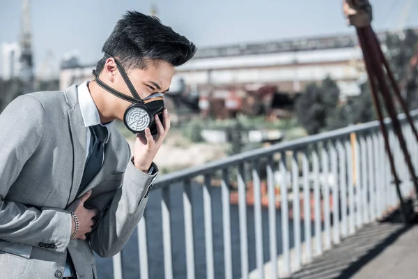 Businessman in protective mask having problem with breathing on bridge, air pollution concept — Stock Photo