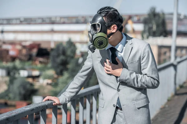 Uomo d'affari in maschera antigas avendo problemi con la respirazione sul ponte, concetto di inquinamento atmosferico — Foto stock