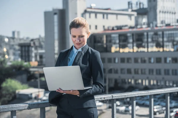 Attractive businesswoman using laptop on bridge — Stock Photo