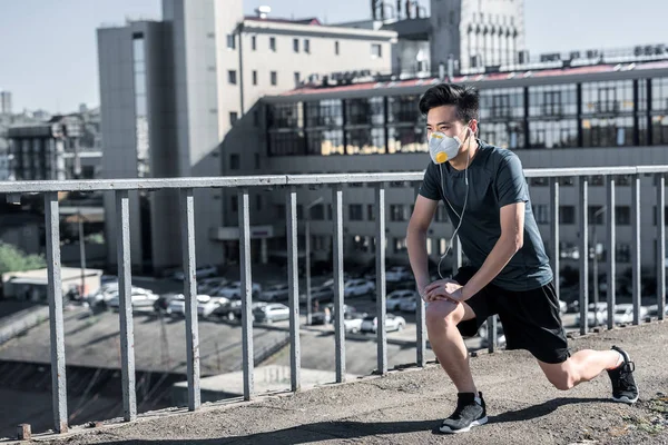 Asian teen stretching legs in protective mask on bridge, air pollution concept — Stock Photo