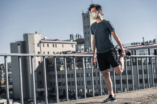 Asian teenager stretching in protective mask on bridge, air pollution concept — Stock Photo