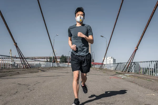 Asian teenager running in protective mask on bridge, air pollution concept — Stock Photo