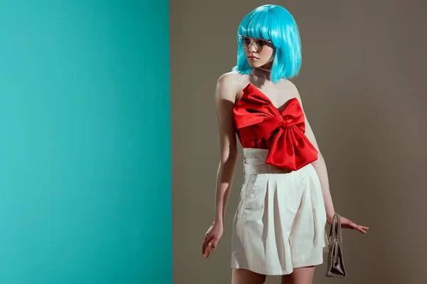 Atractiva joven modelo femenino en peluca azul y lazo rojo mirando hacia otro lado en el estudio - foto de stock