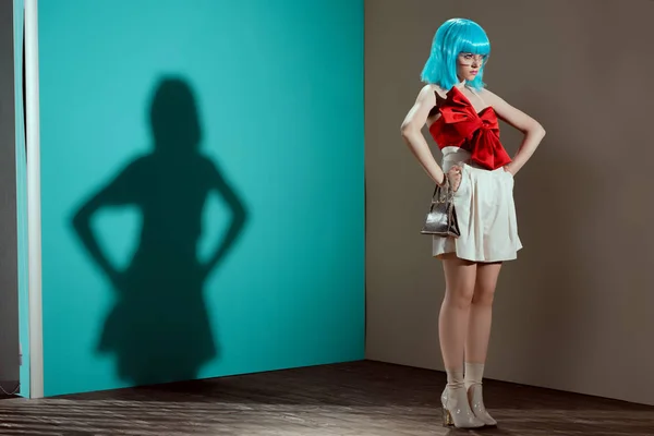 Full length view of beautiful fashionable female model in blue wig posing with hands on waist and looking away — Stock Photo