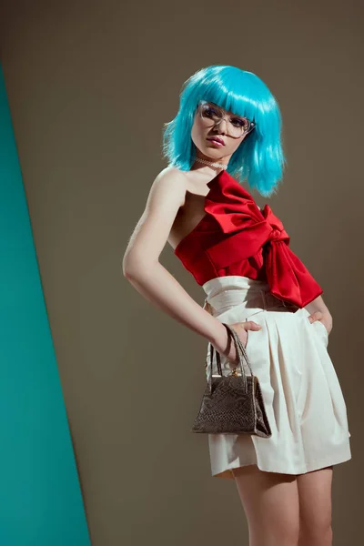 Baixo ângulo de visão de belo modelo feminino em peruca azul em pé com as mãos na cintura em estúdio — Fotografia de Stock