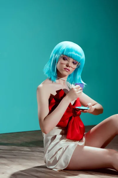 Bella giovane donna in parrucca blu tenendo tazza giocattolo e seduto sul pavimento — Foto stock