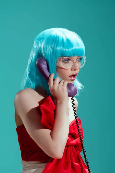Шокована стильна дівчина в синій перуці розмовляє по телефону і дивиться ізольовано на синій — стокове фото