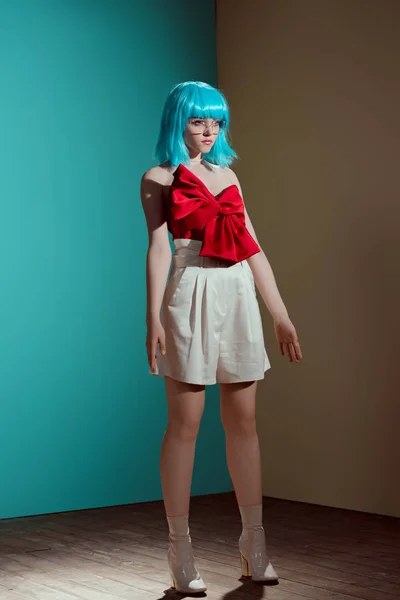 Fashionable female model in blue wig and red bow looking away in studio — Stock Photo