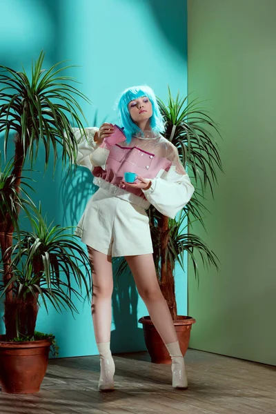 Chica de moda en peluca azul sosteniendo tetera y taza de juguete - foto de stock