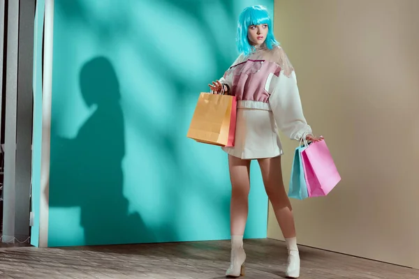 Visão de comprimento total de elegante modelo feminino muito jovem em azul peruca segurando sacos de papel e olhando para longe — Fotografia de Stock