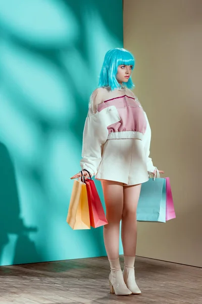 Full length view of fashionable young female model in blue wig holding shopping bags and looking away — Stock Photo