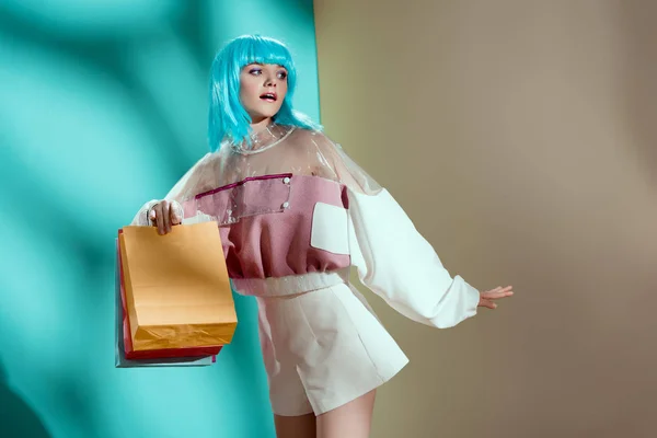 Beautiful stylish young woman in blue wig holding shopping bags and looking away in studio — Stock Photo