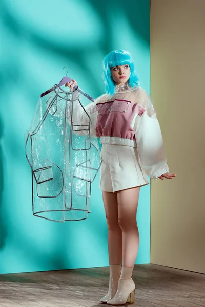 Full length view of stylish female model in blue wig holding transparent raincoat — Stock Photo