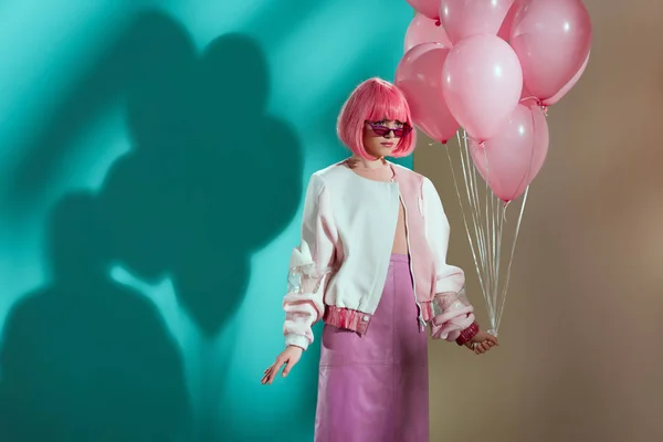 Elegante chica bonita en brillante peluca sosteniendo globos de color rosa y mirando hacia otro lado - foto de stock