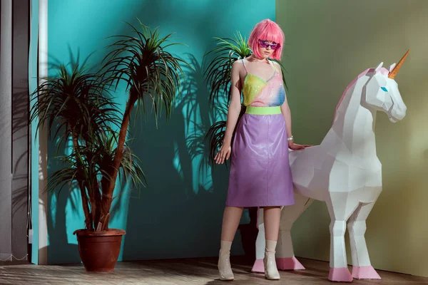 Attractive stylish girl in pink wig standing near unicorn and looking at camera — Stock Photo