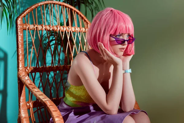 Beau modèle jeune femme à la mode en perruque rose assis dans un fauteuil à bascule et regardant loin — Photo de stock