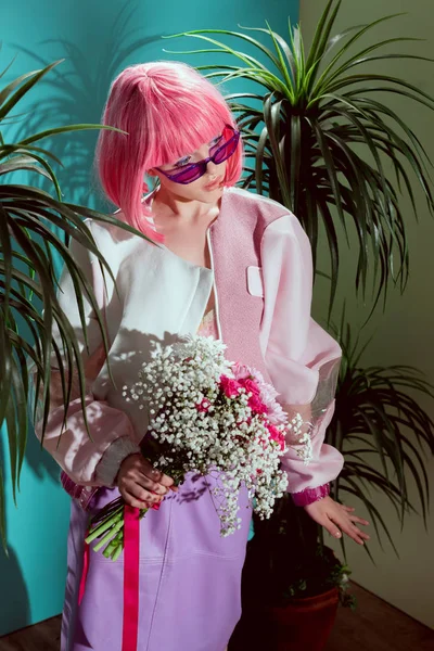 Vista de ángulo alto de la chica de moda en peluca rosa con ramo de flores y mirando hacia otro lado - foto de stock