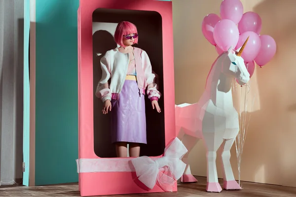 Модель в розовом парике, стоящая в декоративной коробке с луком — стоковое фото