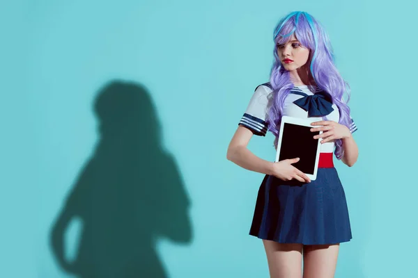 Stylish girl in bright wig holding digital tablet with blank screen and looking away on blue — Stock Photo