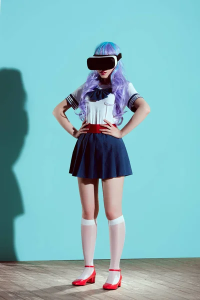 Повнометражний вигляд дівчини в яскравій перуці з використанням гарнітури віртуальної реальності і стоячи з руками на талії на синьому — стокове фото