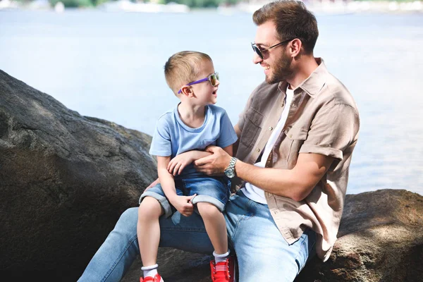 Heureux père et fils regardant les uns les autres sur les pierres au parc — Photo de stock