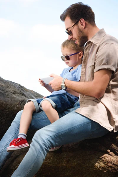 Padre e hijo usando smartphone en piedras en el parque - foto de stock