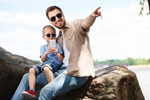 Vater zeigt Sohn mit Smartphone im Park auf etwas — Stockfoto