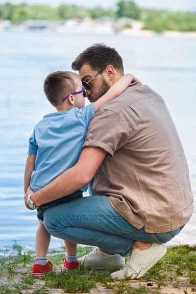Father and son hugging and touching with noses near river at park — Stock Photo