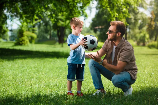 Hijo dando pelota de fútbol a padre en el parque - foto de stock