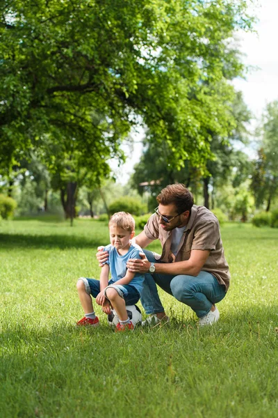 Padre abbracciare e sostenere pianto figlio dopo aver giocato a calcio al parco — Foto stock