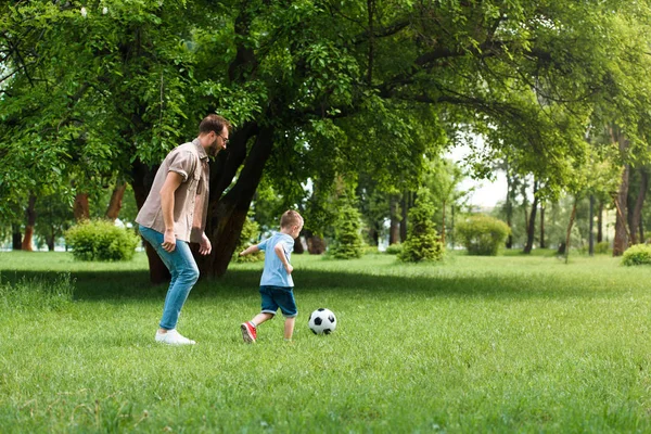 Вид сбоку отца и сына, играющих в футбол в парке — стоковое фото