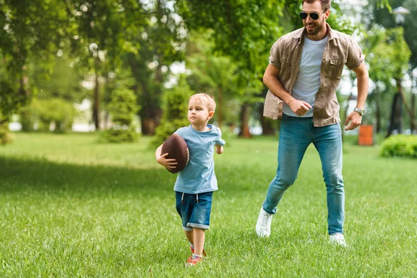 Vater und Sohn laufen mit American-Football-Ball im Park — Stockfoto